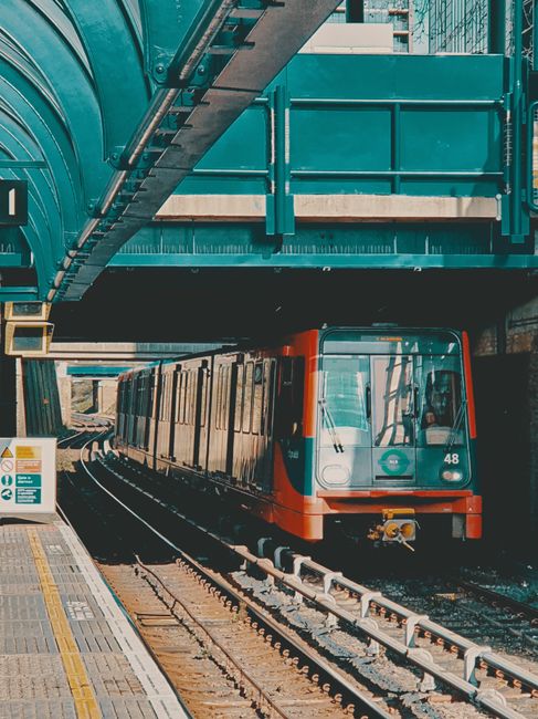 An image showing a modern train with a predominantly grey and red exterior arriving at an urban station platform for house removals and furniture transport. The train is positioned on railway tracks b