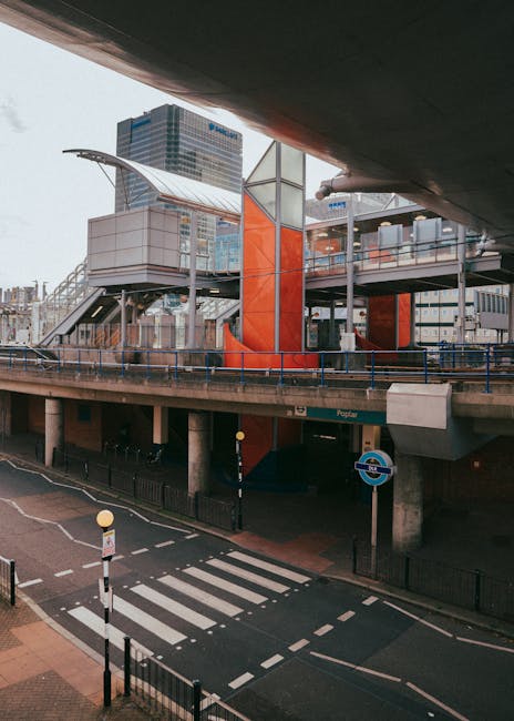 An image showing a modern train with a predominantly grey and red exterior arriving at an urban station platform for house removals and furniture transport. The train is positioned on railway tracks b